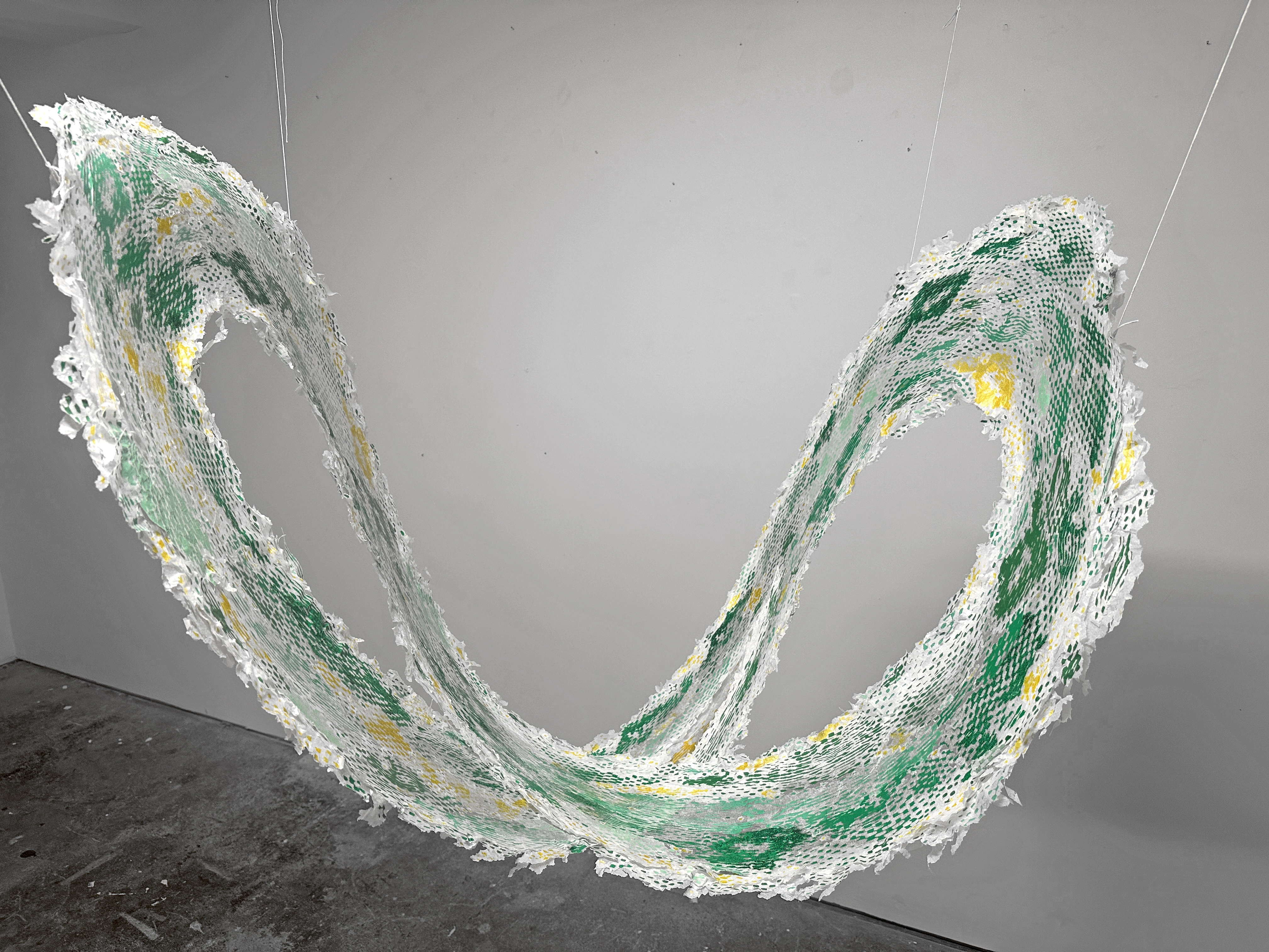 Uncoiling Mature Universe 05.22.26 — a green and yellow screen-print collage suspended as a hanging mobile.